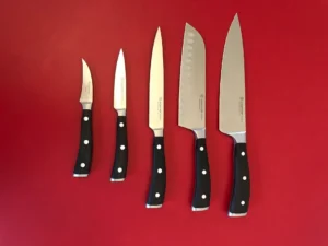Five sharpened Wusthof Ikon kitchen knives lined up from smallest to largest on a red background.