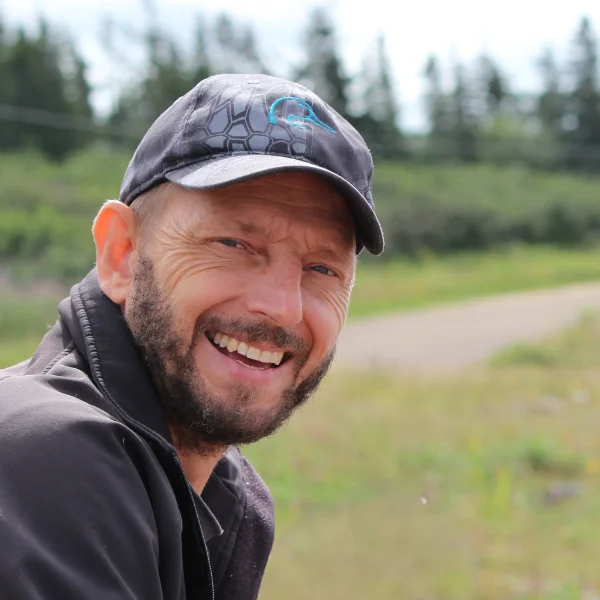 Ken, owner of Maritime Sharpening smiling at the camera. Wearing a black cap and black jacket. In the background some trees and grass.